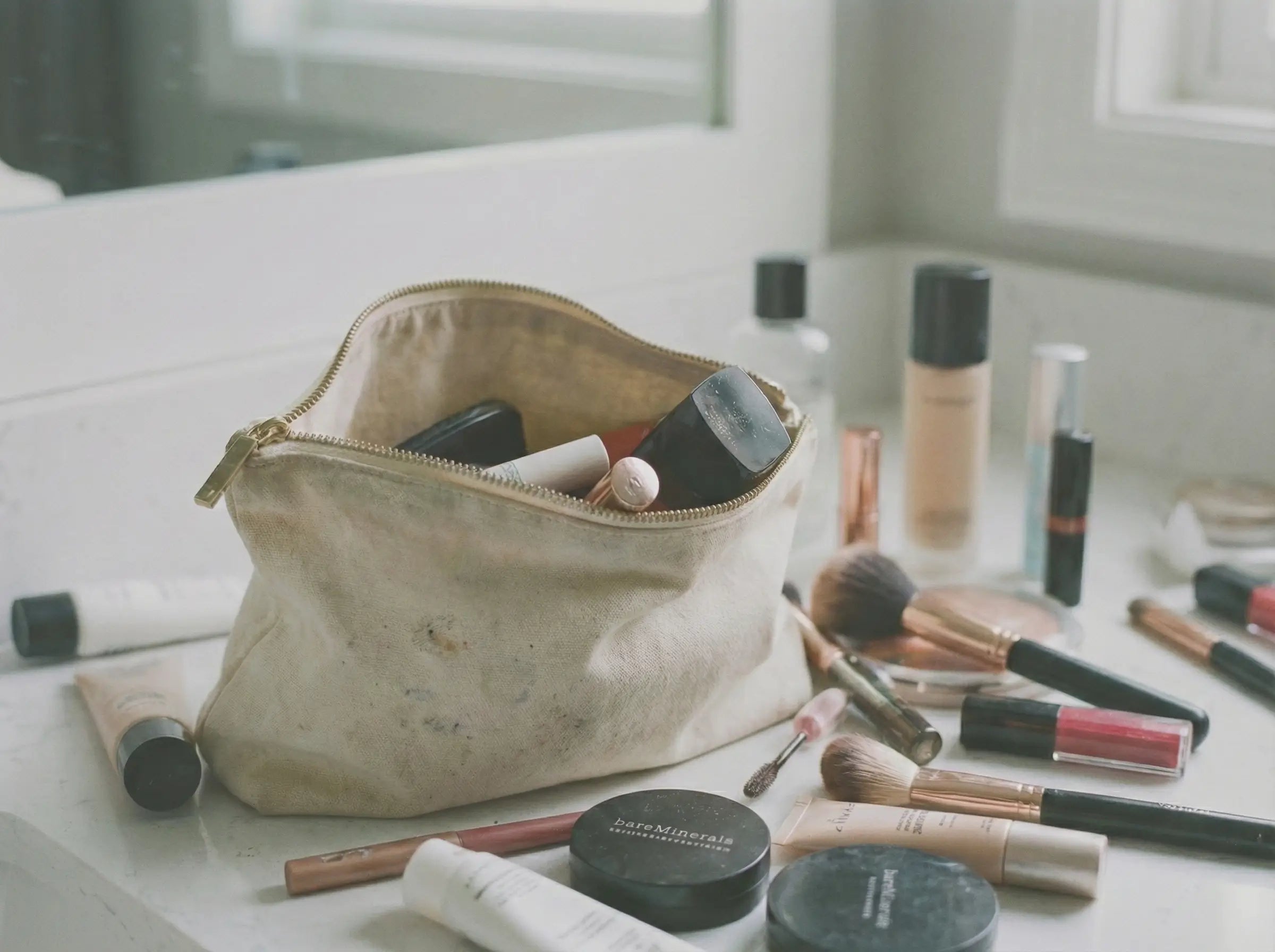 A dirty, unorganized canvas makeup bag overflowing with cluttered cosmetics on a bathroom counter, representing the common struggle of messy beauty routines